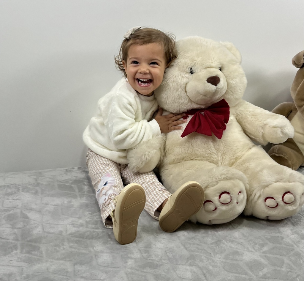 Criança sorrindo abraçada com urso gigante de pelúcia Xikita